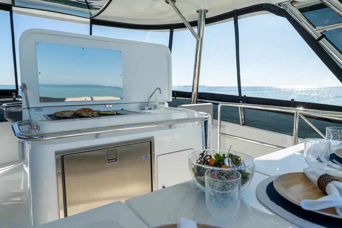 A modern boat's galley with grilled fish, a salad bowl, and scenic ocean views through large windows.